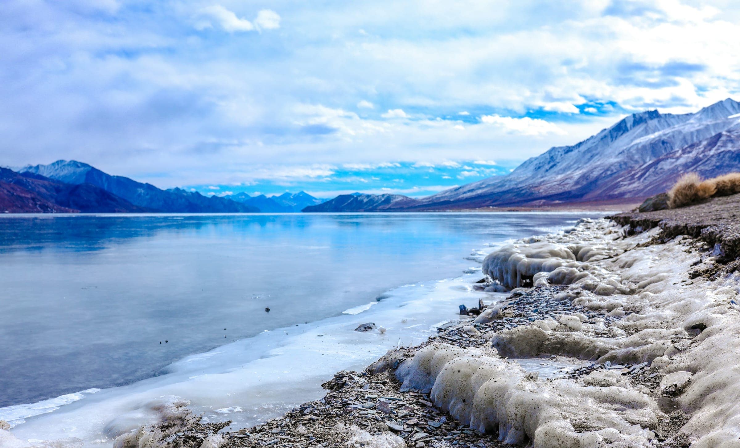 The frozen, ice-edged shoreline of Pangong Lake in Ladakh, ringed by snow-dusted mountains